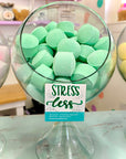 Glass bowl filled with green shower fizzies with a 'Stress Less' sign.
