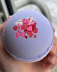 Bath bomb with colorful design held in a hand against a blurred background