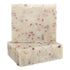 A bar of soap with a light color and embedded with bits of oats, displayed against a white background.